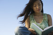 Woman reading book outdoors, hair blowing in breeze
