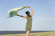 Woman standing outdoors, holding up shawl in wind, full length