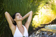 Woman relaxing by waterfall with hands behind head