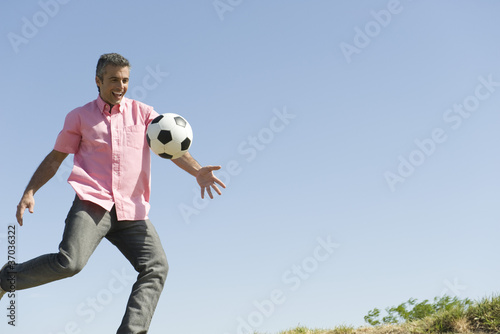 Photo: Man playing with soccer ball outdoors, smiling Man playing with soccer ball outdoors, smiling