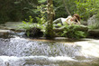 Young woman relaxing on rock by flowing stream