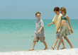 Three children walking next to surf on beach