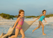 Two girls running on beach, holding blanket out in wind