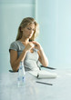 Woman sitting at table with pad of paper, pen and bottle of water, looking down
