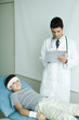 Photo: Boy lying on examination table with bandage on forehead and arm, doctor writing on clipboard Boy lying on examination table with bandage on forehead and arm, doctor writing on clipboard