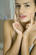 Young woman applying facial mask, looking at camera, cropped view