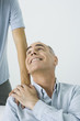 Mature man holding son's hand on shoulder, smiling up over shoulder, cropped view