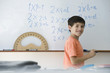 Elementary school student writing equations on whiteboard, smiling over shoulder at camera