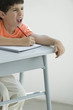 Elementary school student taking notes in classroom, squinting at board