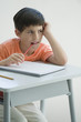 Elementary school student sitting at desk, leaning on elbow, chewing end of pencil