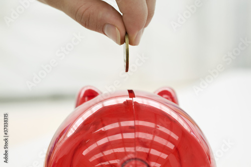 Photo: Person placing coin in piggy bank, close-up Person placing coin in piggy bank, close-up
