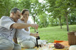 Mature couple having picnic outdoors, opening bottle of wine