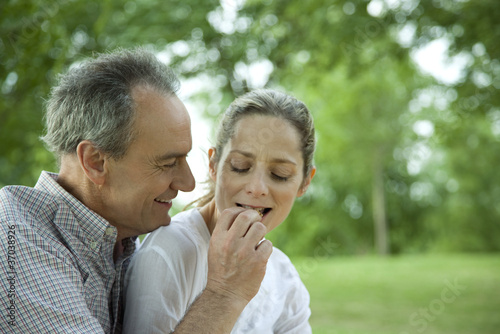 Foto: Mature couple together in park, man feeding woman Mature couple together in park, man feeding woman
