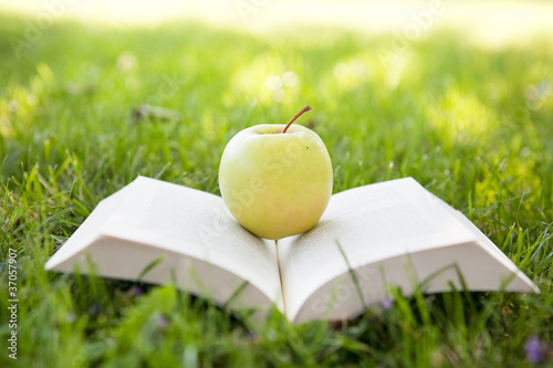 Photo: Open book and apple on tre grass Open book and apple on tre grass
