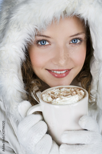 Foto: A woman wearing a winter coat, holding a mug of hot chocolate A woman wearing a winter coat, holding a mug of hot chocolate