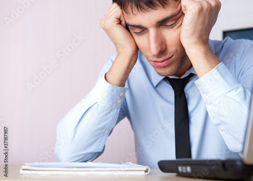 Photo: Tired businessman sleeping at his desk in the office with both a Tired businessman sleeping at his desk in the office with both a