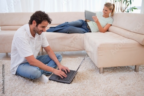 Photo: Woman using a tablet computer while her boyfriend is using a lap Woman using a tablet computer while her boyfriend is using a lap