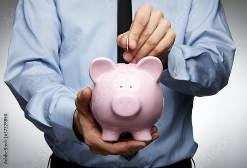Foto: Male hand putting coin into a piggy bank Male hand putting coin into a piggy bank