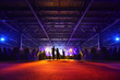 People stand, sit at table and look at illuminated stage