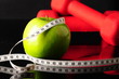 apple, tapeline and dumbbells on black