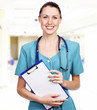 Doctor in hospital corridor holding clipboard and smiling to you