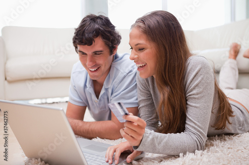 Foto: Couple lying on the floor with laptop booking holidays Couple lying on the floor with laptop booking holidays