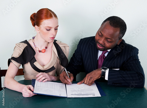 Photo: Black man and redhead young woman sitting with documentation Black man and redhead young woman sitting with documentation