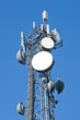 Cell tower and radio antenna in trees against a blue sky