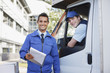 Worker with clipboard standing with truck and driver