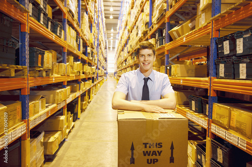 Photo: Worker standing in warehouse with box Worker standing in warehouse with box