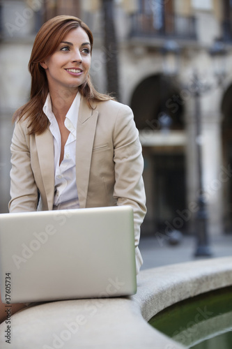 Photo: Businesswoman sitting by fountain using internet Businesswoman sitting by fountain using internet