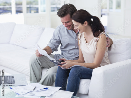 Photo: Couple sitting on sofa paying bills together Couple sitting on sofa paying bills together