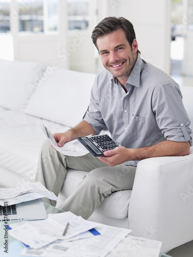 Photo: Man sitting on sofa paying bills Man sitting on sofa paying bills