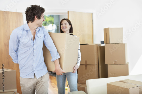 Photo: Couple carrying moving boxes into new home Couple carrying moving boxes into new home