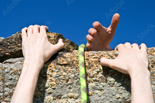 Photo: Rock climber reaching for helping-hand partner. Rock climber reaching for helping-hand partner.