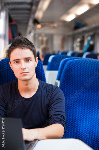 Photo: Handsome young man using his laptop computer while on the train Handsome young man using his laptop computer while on the train