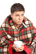 Ill man holding a tea cup and a thermometer in his mouth