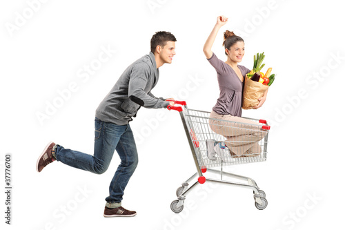 Photo: Person pushing a happy woman in a shopping cart with paper bag f Person pushing a happy woman in a shopping cart with paper bag f