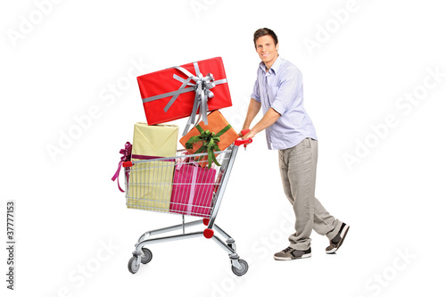 Photo: Young man pushing a shopping cart full with gifts Young man pushing a shopping cart full with gifts