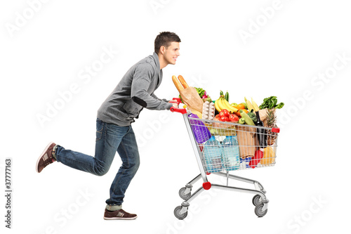 Photo: Young man running and pushing a shopping cart full with food Young man running and pushing a shopping cart full with food