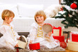 Two smiling twins girl opening presents near Christmas tree