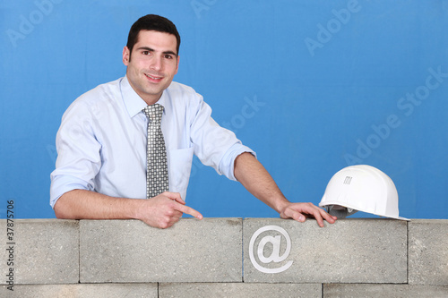 Photo: businessman pointing at an at sign on a wall businessman pointing at an at sign on a wall