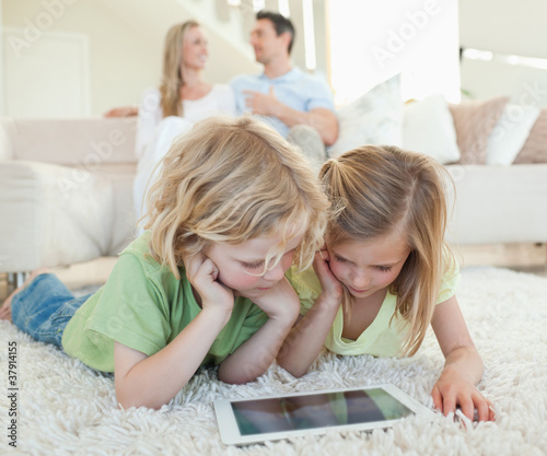 Photo: Children on the floor with tablet and parents behind them Children on the floor with tablet and parents behind them