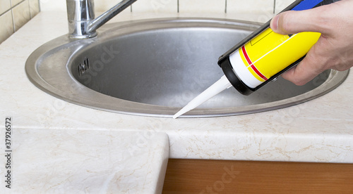 Photo: Plumber putting a silicone sealant to installing a kitchen sink Plumber putting a silicone sealant to installing a kitchen sink