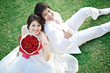 portrait of bride and groom sitting on fresh grass with rose bou