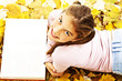 Teenage girl lying down reading book with leaves around.