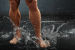 Strong legs of undressed tanned bodybuilder make water spray