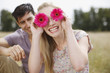 Portrait of playful woman holding flowers over eyes in rural field