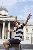 Photo: Portrait of exuberant woman with arms outstretched sliding on railing in front of historical landmark Portrait of exuberant woman with arms outstretched sliding on railing in front of historical landmark