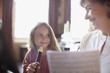 Grandmother with sheet music watching granddaughter practice on recorder